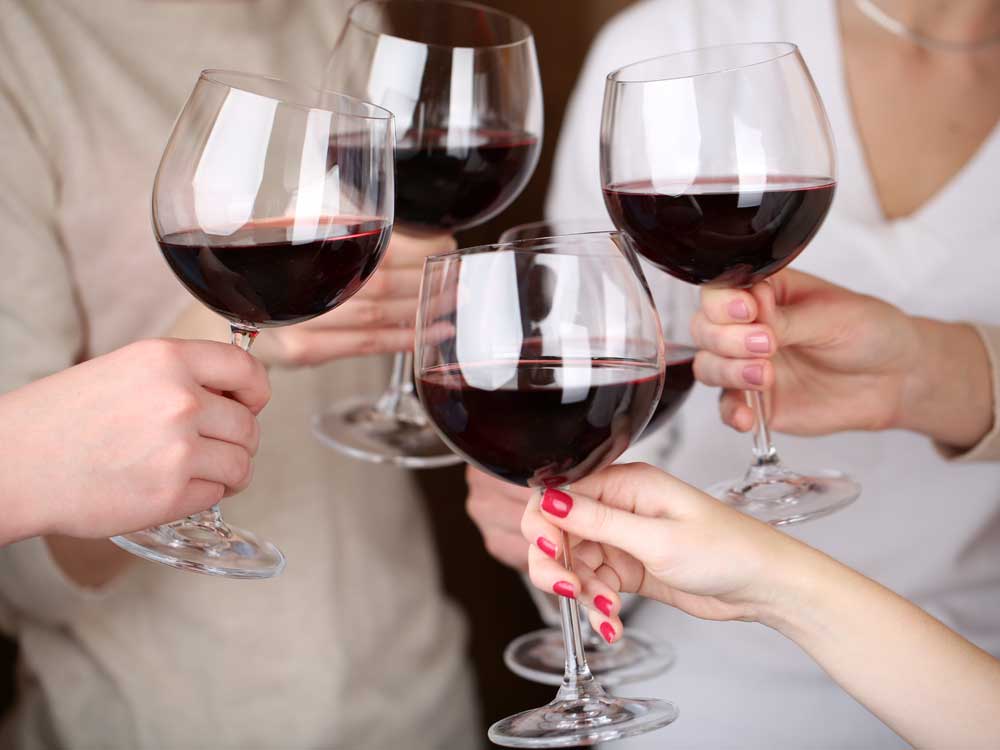 four people toasting with large glasses of red wine