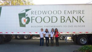 Four people standing under the logo on the side of a Redwood Empire Food Bank truck