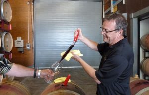 Winemaker shares a taste of Pinot Noir directly from the barrel by using a wine thief.