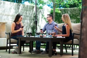 Two woman and a man enjoy a food and wine pairing in a courtyard area.