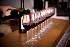 line of glasses being poured with red wine