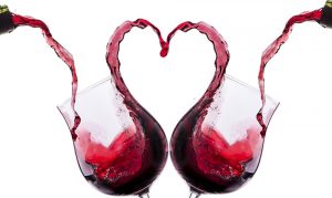 Red wine being poured into two glasses and forming a heart as it splashing out the other side.