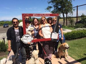 Group of people with dogs on leashes doing a selfie with a #DrinkBalletto - WineRoad frame