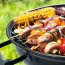 A kettle barbecue grill filled with kebabs of meat and veggies, plus corn on the cob