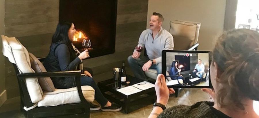 Woman and man talking over a glass of wine as a third person makes a video of them.