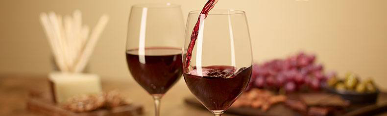 Red wine being poured into nice wine glasses with food in the background.