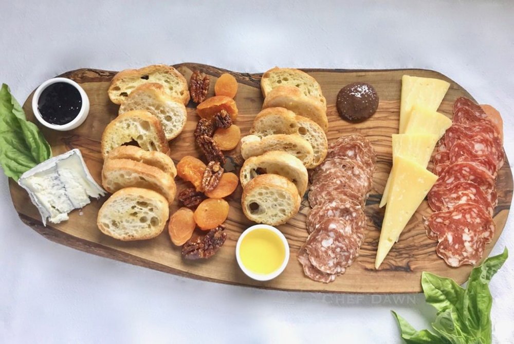 Charcuterie board with meats, cheeses, bread, dried apricots, pecans, olive oil and sauces