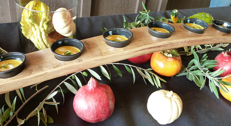 Sample of butternut squash soup surrounded by a decorative fall display with gourds, pomegranates and olive branches