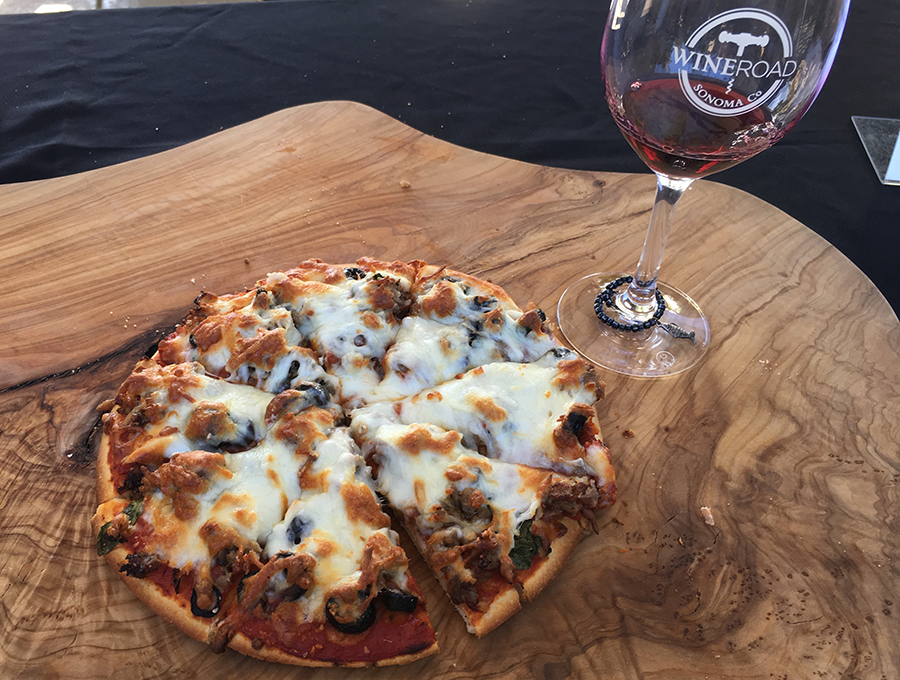 A pizza with a Wine Road logo glass on the side.