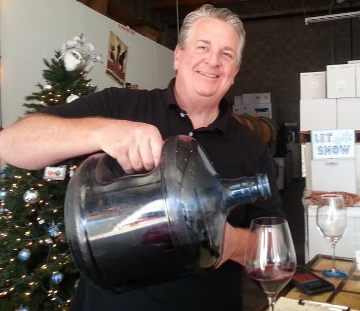 Craig Colagrossi pouring red wine out of a plastic jug into a wine glass.