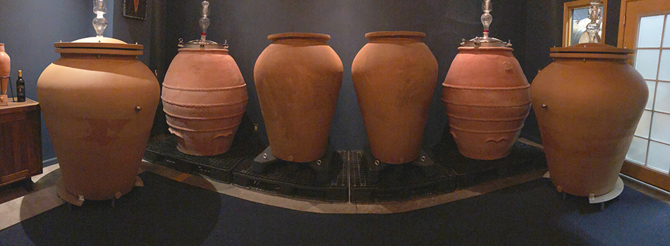 Six large amphoras, or wine vessels, lined up inside a room.