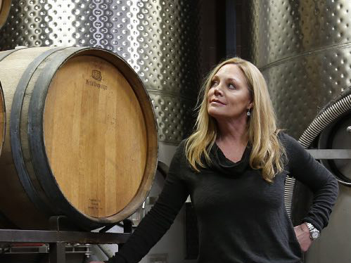 Susie Selby standing by a oak wine barrel with stainless steel tanks in the background.