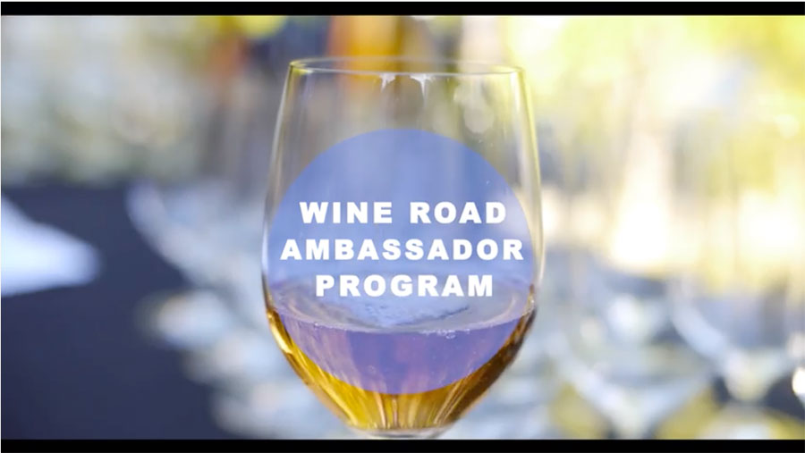 A glass of white wine with the words Wine Road Ambassador Program over the top of the glass.